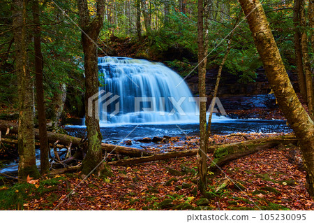 Gorgeous large blue waterfall and river with cliff walls, forest, fallen leaves and trees, clearing Gorgeous large blue waterfall and river with cliff walls, forest, fallen leaves and trees, clearing 105230095