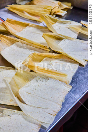 Vertical of silver tray of several pre-baked tamales with masa and corn husk exposed Vertical of silver tray of several pre-baked tamales with masa and corn husk exposed 105230176
