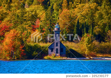 Lighthouse with boarded up windows on a distant shore colorful fall trees and sapphire lake water Lighthouse with boarded up windows on a distant shore colorful fall trees and sapphire lake water 105230177