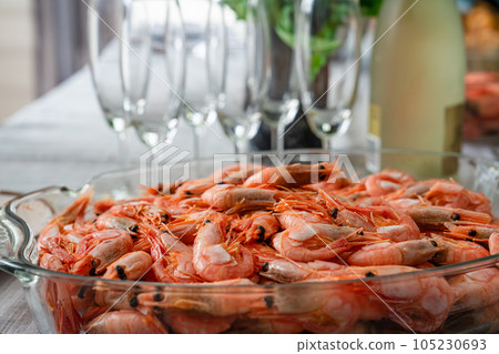 A dish of unpeeled shrimp on a dinner table with plates. Seafood diner. Boiled shrimps. 105230693