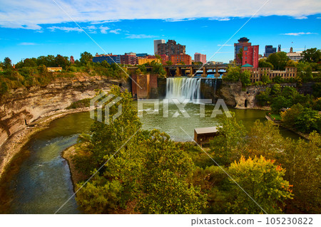 Rochester skyline along river and cliffs with waterfall pouring past bridge 105230822