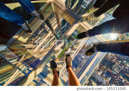 Looking down on glass floor elevator New York City with three pairs of tourist feet and balcony below 105231000
