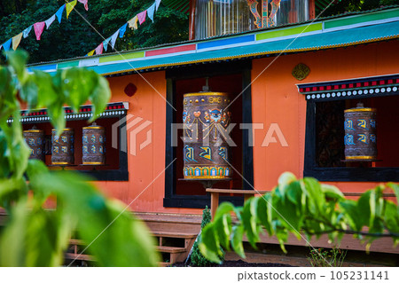Temple with ornate prayer wheels through the leaves Temple with ornate prayer wheels through the leaves 105231141