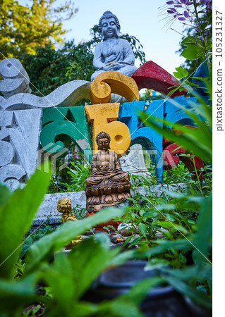 View of small buddha statues through garden plants 105231327