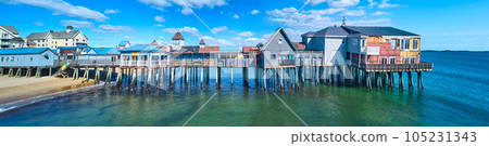 Stunning side profile of entire old wood pier in Maine covered in shops and buildings on beach 105231343