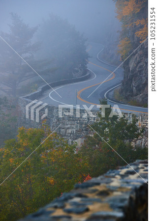 Foggy morning detail of winding road through cliffs with beautiful stone wall 105231554