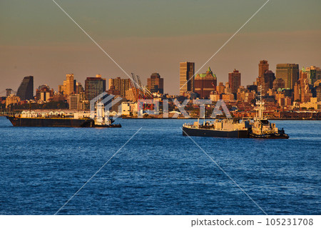 Pair of industrial merchant ships in New York City bay in golden hour with city behind Pair of industrial merchant ships in New York City bay in golden hour with city behind 105231708
