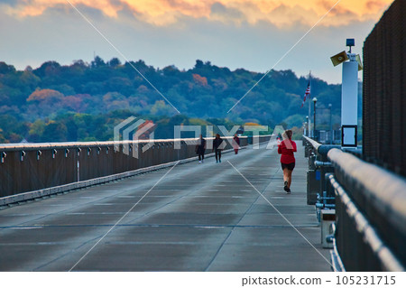 Joggers running along long cement bridge boardwalk with forests in background 105231715
