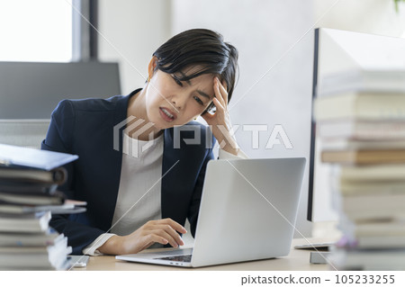 Desk work A business woman holding her head while looking at the screen of a laptop computer 105233255