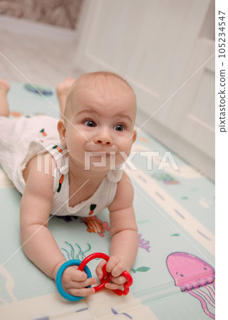 A cute baby in a white suit sits on a soft mat and plays with bright toys. High quality photo A cute baby in a white suit sits on a soft mat and plays with bright toys. High quality photo 105234547