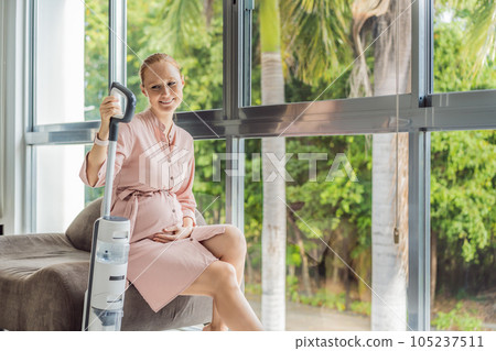 Young pregnant woman enjoys cleaning her house. Easy cleaning with a wireless vacuum cleaner. Pregnant woman cleaning floor with handheld vacuum cleaner. Modern easy cleaning Young pregnant woman enjoys cleaning her house. Easy cleaning with a wireless vacuum cleaner. Pregnant woman cleaning floor with handheld vacuum cleaner. Modern easy cleaning 105237511