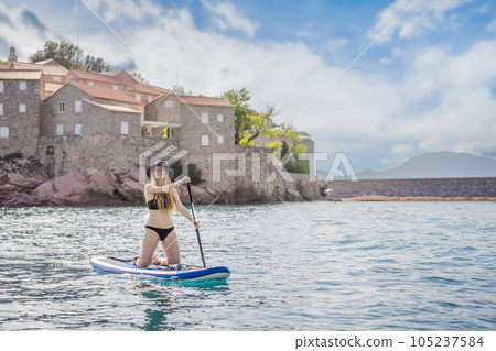Young women Having Fun Stand Up Paddling in blue water sea near st stefan island in Montenegro. SUP 105237584