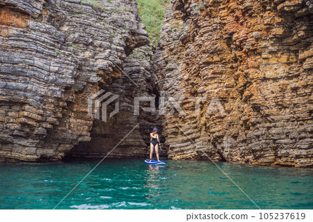 Young women Having Fun Stand Up Paddling in blue water seaamong the rocks in Montenegro. SUP 105237619