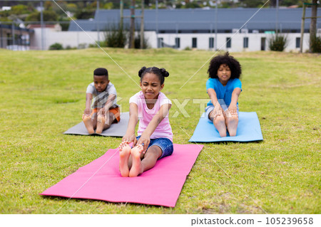 Happy african american schoolchildren doing yoga and stretching on field at school 105239658