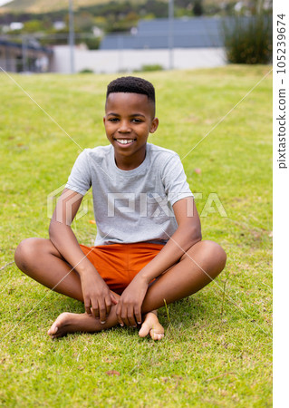 Portrait of happy african american schoolboy sitting on grass at school 105239674