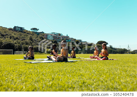 Diverse schoolgirls practicing yoga meditation on sunny elementary school sports field Diverse schoolgirls practicing yoga meditation on sunny elementary school sports field 105240478