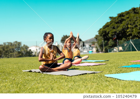 Focused diverse schoolgirls practicing yoga and meditating at stadium on sunny day Focused diverse schoolgirls practicing yoga and meditating at stadium on sunny day 105240479