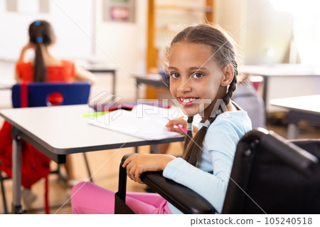 Portrait of happy diverse and disabled schoolgirls in wheelchair writing in classroom 105240518