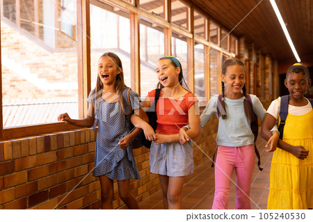 Diverse happy schoolgirls with bags walking and embracing in elementary school corridor Diverse happy schoolgirls with bags walking and embracing in elementary school corridor 105240530