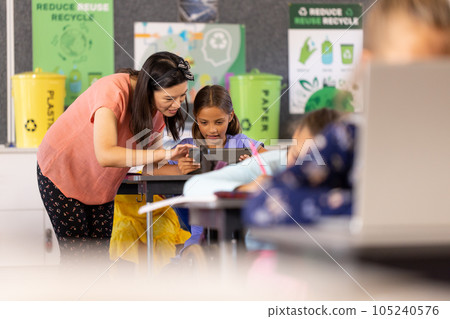 Happy diverse female teacher teaching schoolgirls using tablet in classroom 105240576