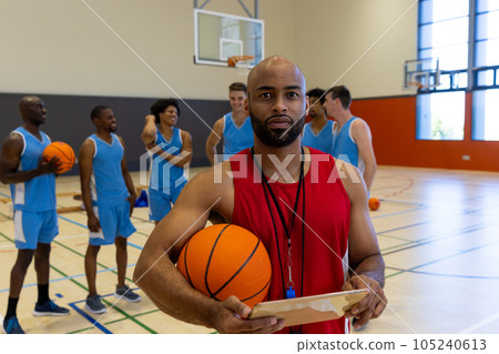 Portrait of biracial male coach with tablet over happy male basketball players talking at gym 105240613