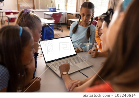 Diverse female teacher with laptop and elementary schoolgirls in class, copy space 105240614