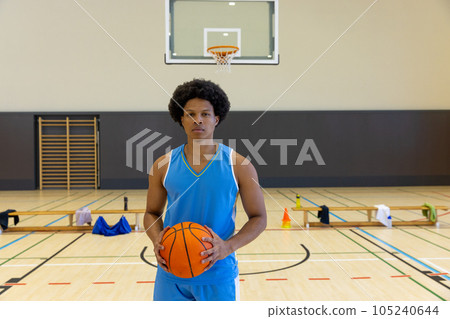 Portrait of biracial male basketball player with basketball wearing blue sports clothes at gym 105240644