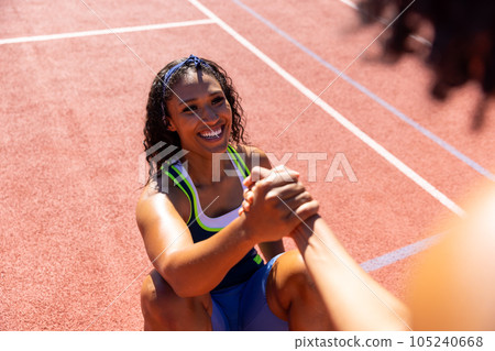 Happy biracial female friends holding hands and helping to get up at basketball court Happy biracial female friends holding hands and helping to get up at basketball court 105240668