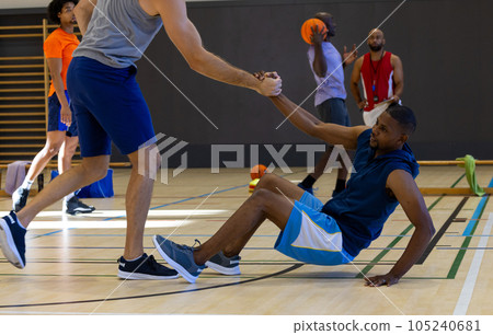 Diverse male basketball players helping to get up with coach at gym 105240681
