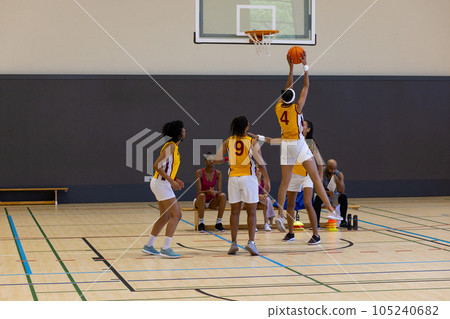 Focused diverse female basketball players with male coach playing basketball at gym 105240682
