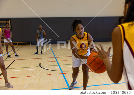 Focused biracial female basketball players with male coach playing basketball at gym 105240683