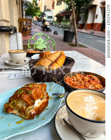 Turkish breakfast with menemen and kaymak croissant on a table of a street cafe. High quality photo Turkish breakfast with menemen and kaymak croissant on a table of a street cafe. High quality photo 105241370