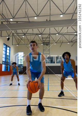 Diverse male basketball players wearing blue sports clothes and shooting basketball at gym 105242292