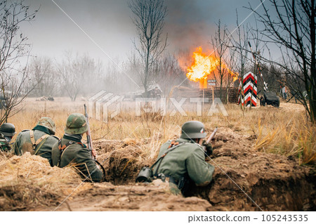 Re-enactors Dressed As World War Ii German Wehrmacht Infantry Soldiers Fighting Defensively In Trench. Defensive Position. Smokescreen. Building On Fire On Background 105243535