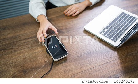 Charging mobile phone battery with wireless charging device in the table. Smartphone charging on a charging pad. Mobile phone near wireless charger Modern lifestyle technology concept. Charging mobile phone battery with wireless charging device in the table. Smartphone charging on a charging pad. Mobile phone near wireless charger Modern lifestyle technology concept. 105246172
