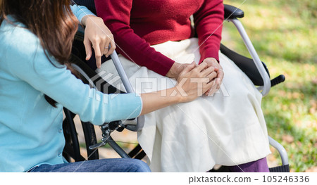 Family relationship Asian senior woman in wheelchair with happy daughter holding caregiver for a hand while spending time together Family relationship Asian senior woman in wheelchair with happy daughter holding caregiver for a hand while spending time together 105246336