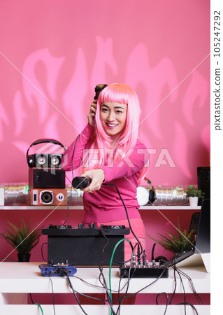 Asian musical artist playing electronic music using mixer console while hold out the microphone to fans, enjoying dacing together and having fun. Dj woman performing at night in club 105247292
