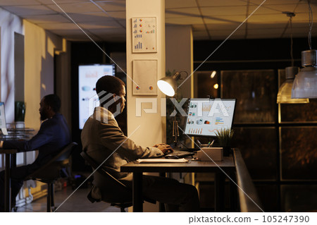 Businessman checking marketing report on computer, analyzing financial graphs while working overhours at company strategy. African american manager planning management research plan 105247390
