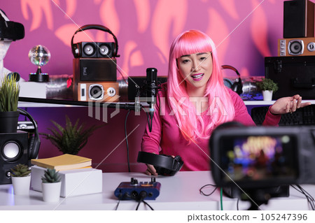 Portrait of smiling content creator sitting at desk table recording podcast talking into microphone with subscribers discussing lifestyle advice. Cheerful woman filming vlog using vlogging equipment 105247396