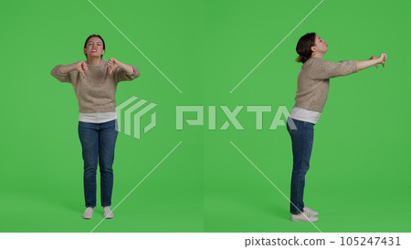Female model showing thumbs down negative sign on camera, doing disapproval and bad symbol. Confident woman expressing disagreement with dislike gesture over full body greenscreen. 105247431
