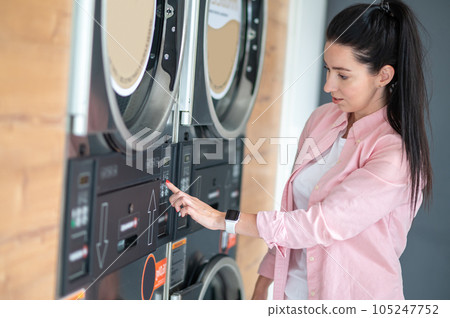Young woman pressing button in washing machine at public laundry. Young woman pressing button in washing machine at public laundry. 105247752
