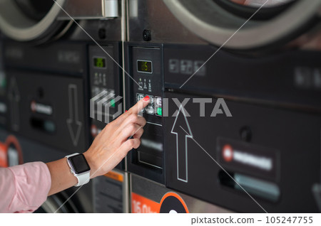 Young woman pressing button in washing machine at public laundry. 105247755
