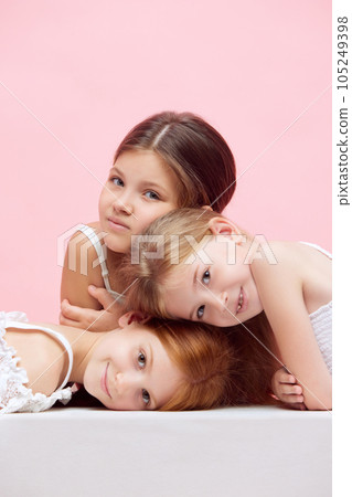 Portrait of little beautiful children, girls posing together against pink studio background. Well-being Portrait of little beautiful children, girls posing together against pink studio background. Well-being 105249398