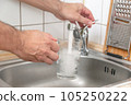 Filling a glass with tap water for drinking by holding it in man hand at the sink in the kitchen 105250222