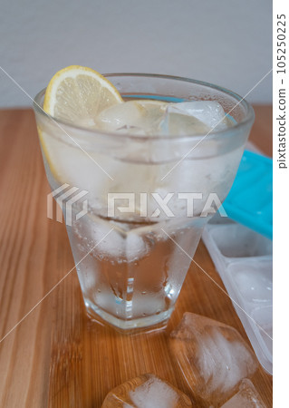 Sparkling water with bubbles in a big transparent glass filled with ice cubes and lemon, a soft plastic form to make ice cubes in the freezer. Solution to overcome extreme high temperature in summer 105250225
