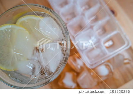 Sparkling water with bubbles in a big transparent glass filled with ice cubes and lemon, a soft plastic form to make ice cubes in the freezer. Solution to overcome extreme high temperature in summer Sparkling water with bubbles in a big transparent glass filled with ice cubes and lemon, a soft plastic form to make ice cubes in the freezer. Solution to overcome extreme high temperature in summer 105250226