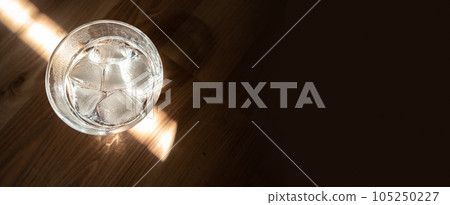 Banner with sparkling water with bubbles in a big transparent glass filled with ice cubes with copy space solid background. Solution to overcome extreme high temperature in summer Banner with sparkling water with bubbles in a big transparent glass filled with ice cubes with copy space solid background. Solution to overcome extreme high temperature in summer 105250227