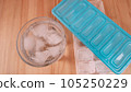 Sparkling water with bubbles in a big transparent glass filled with ice cubes and a soft plastic blue form to make ice cubes in the freezer. Solution to overcome extreme high temperature in summer 105250229
