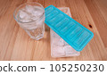 Sparkling water with bubbles in a big transparent glass filled with ice cubes and a soft plastic blue form to make ice cubes in the freezer. Solution to overcome extreme high temperature in summer 105250230