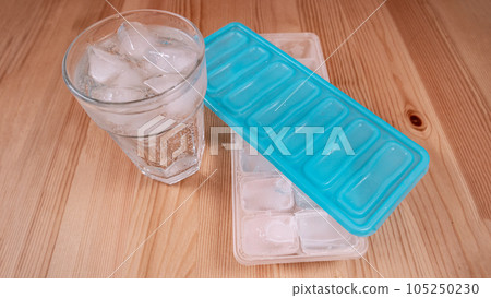 Sparkling water with bubbles in a big transparent glass filled with ice cubes and a soft plastic blue form to make ice cubes in the freezer. Solution to overcome extreme high temperature in summer 105250230